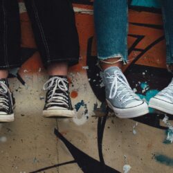 des pieds avec des chaussures converses près d'un mur avec graffitis