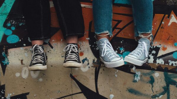 des pieds avec des chaussures converses près d'un mur avec graffitis